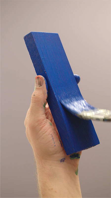 Een houten blokje met blauwe verf en een kwast die dit aanbrengt